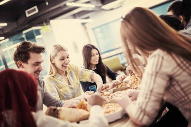 Farklı etnik çeşitlilikte dost canlısı iş adamları başlangıç ofisinde pizzalarını paylaşıyor, çok ırklı iş arkadaşları grubu öğle yemeği arasında eğleniyor ve gülüyor.
