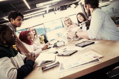 Yeni iş planlarını tartışan, laptop ve tablet bilgisayarlar üzerinde çalışan çok ırklı bir girişim ekibi yeni iş geliştirme teknolojileri hakkında bilgi toplarken,