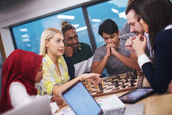 Çok ırklı bir iş adamı grubu modern bir ofis kurarken satranç oynuyor.