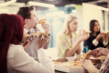 Farklı etnik çeşitlilikte dost canlısı iş adamları başlangıç ofisinde pizzalarını paylaşıyor, çok ırklı iş arkadaşları grubu öğle yemeği arasında eğleniyor ve gülüyor.