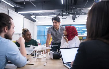 Yeni iş planlarını tartışan, laptop ve tablet bilgisayarlar üzerinde çalışan çok ırklı bir girişim ekibi yeni iş geliştirme teknolojileri hakkında bilgi toplarken,