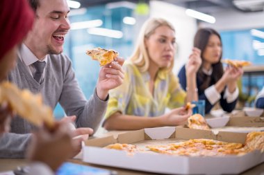 Farklı etnik çeşitlilikte dost canlısı iş adamları başlangıç ofisinde pizzalarını paylaşıyor, çok ırklı iş arkadaşları grubu öğle yemeği arasında eğleniyor ve gülüyor.