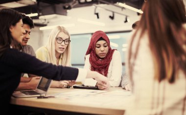 Modern parlak ofis içi beyin fırtınasında toplanan çok ırklı girişim ekibi dizüstü bilgisayar ve tablet bilgisayar üzerinde çalışıyor