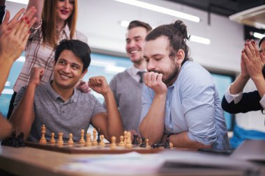 Çok ırklı bir iş adamı grubu modern bir ofis kurarken satranç oynuyor.