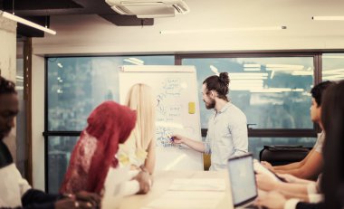 Modern parlak ofis içi beyin fırtınasında toplanan çok ırklı girişim ekibi dizüstü bilgisayar ve tablet bilgisayar üzerinde çalışıyor