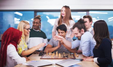 Çok ırklı bir iş adamı grubu modern bir ofis kurarken satranç oynuyor.