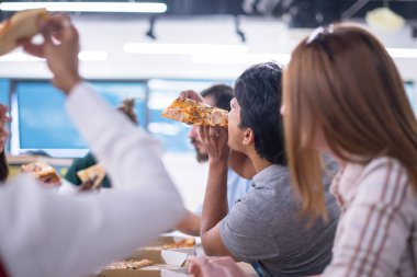 Farklı etnik çeşitlilikte dost canlısı iş adamları başlangıç ofisinde pizzalarını paylaşıyor, çok ırklı iş arkadaşları grubu öğle yemeği arasında eğleniyor ve gülüyor.