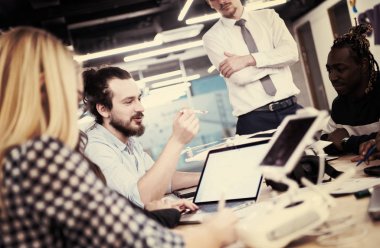 Yeni iş planlarını tartışan, laptop ve tablet bilgisayarlar üzerinde çalışan çok ırklı bir girişim ekibi yeni iş geliştirme teknolojileri hakkında bilgi toplarken,