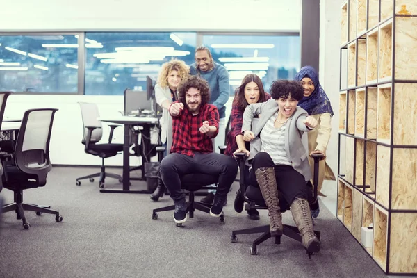 사무실 의자 위에서 레이스를 벌이고 있는 다 민족 사업 팀 — 스톡 사진