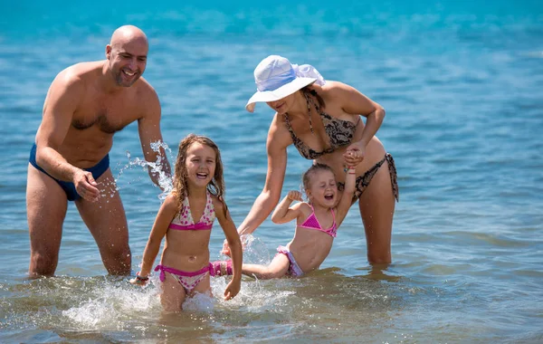 Família feliz salpicando uns aos outros na praia — Fotografia de Stock