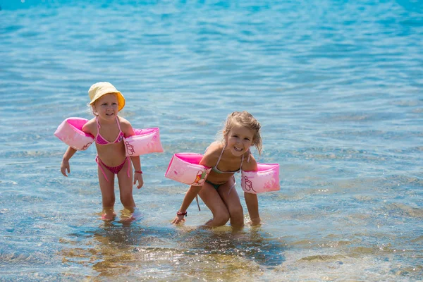 Kleine Mädchen mit Schwimmarmbinden spielen im flachen Wasser — Stockfoto