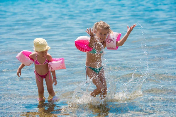 Kleine Mädchen mit Schwimmarmbinden spielen im flachen Wasser — Stockfoto