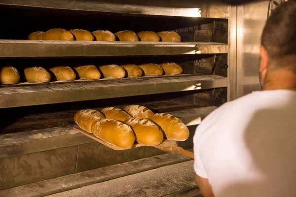 Bakkerij medewerker die versgebakken broodjes uitneemt — Stockfoto