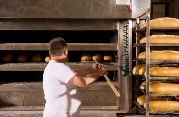 Pracownik piekarni zabierając świeżo pieczone pieczywo — Zdjęcie stockowe