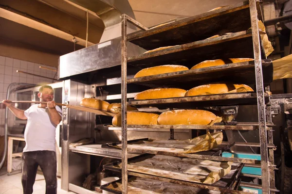 Sütőipari munkás, frissen sült kenyerek vételével — Stock Fotó
