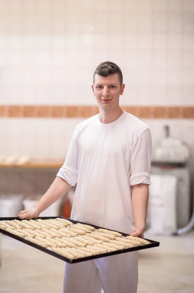 Un giovane panettiere con in mano un prodotto grezzo di pasta bianca — Foto Stock
