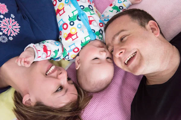 Visão superior do jovem casal sorridente deitado com seu bebê — Fotografia de Stock