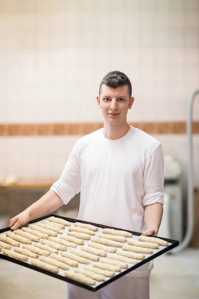 Um padeiro jovem segurando produto cru de massa branca — Fotografia de Stock