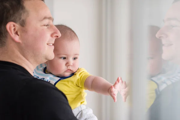 Ung far som håller barnet nära fönstret hemma — Stockfoto