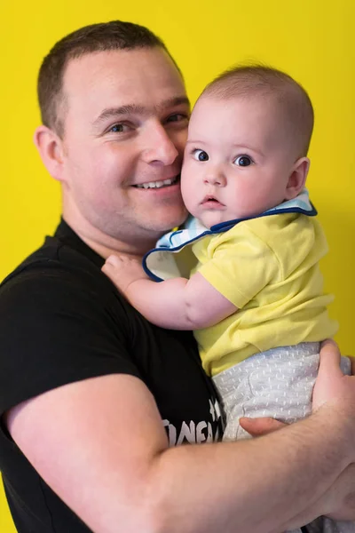 Retrato de feliz padre joven sosteniendo bebé aislado en amarillo —  Fotos de Stock