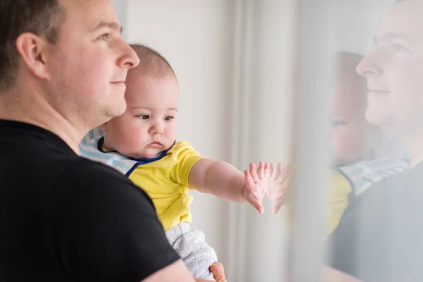 Mladý otec drží dítě u okna doma — Stock fotografie