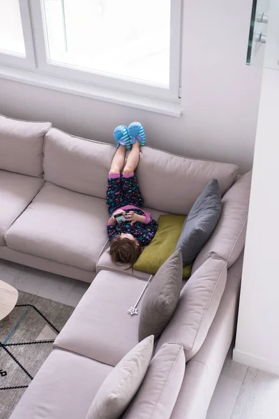 Маленька дівчинка використовує смартфон на дивані вдома — стокове фото