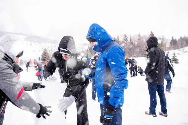 Skupina mladých lidí dělá sněhuláka — Stock fotografie