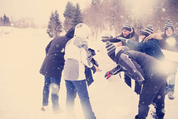 Skupina mladých lidí dělá sněhuláka — Stock fotografie