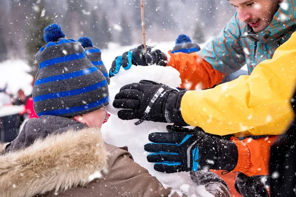 Grupo de jóvenes haciendo un muñeco de nieve —  Fotos de Stock