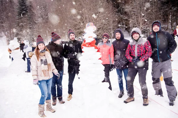 Skupinový portrét mladých lidí pózujících se sněhulákem — Stock fotografie