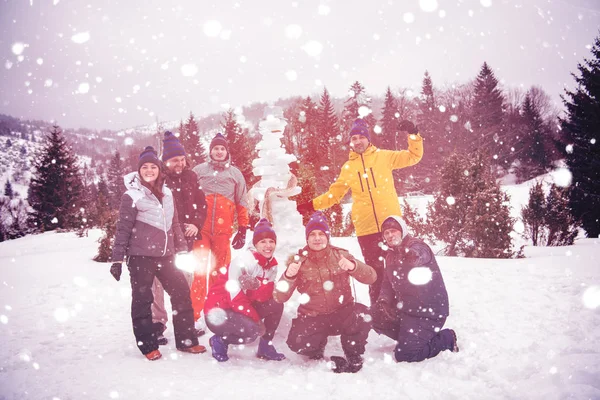 Group portait of young people posing with snowman — Stock Photo, Image