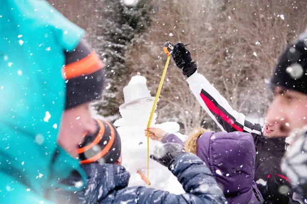 Jóvenes midiendo la altura del muñeco de nieve terminado — Foto de Stock