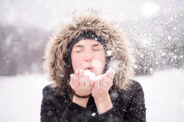Junge Frau pustet Schnee an einem verschneiten Tag — Stockfoto