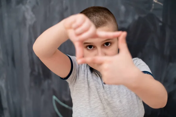 Niño feliz haciendo gesto de marco de mano delante de pizarra — Foto de Stock