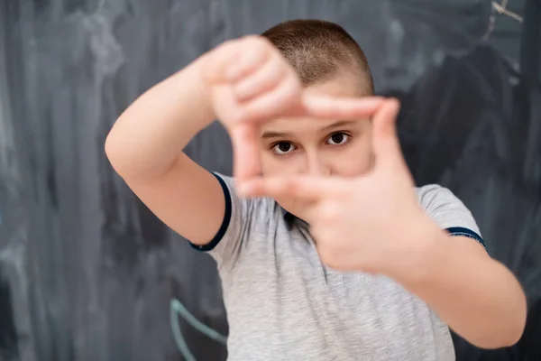 Niño feliz haciendo gesto de marco de mano delante de pizarra — Foto de Stock