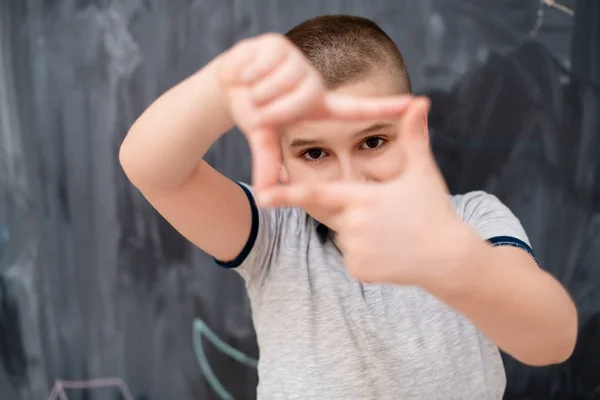 Niño feliz haciendo gesto de marco de mano delante de pizarra — Foto de Stock