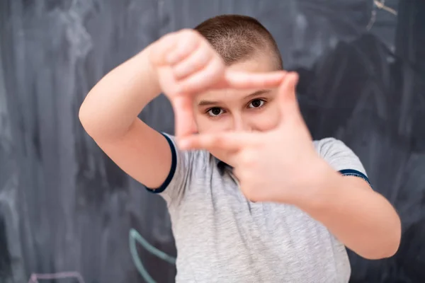 Niño feliz haciendo gesto de marco de mano delante de pizarra —  Fotos de Stock