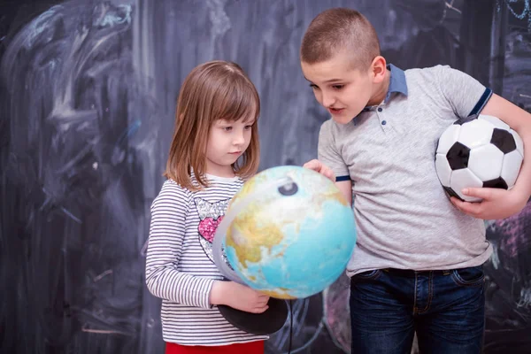 Boy and little girl using globe of earth in front of chalkboard — Stock Photo, Image