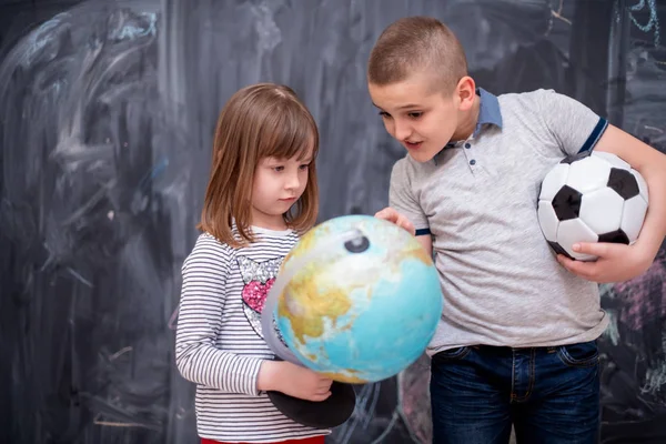 Boy and little girl using globe of earth in front of chalkboard — Stock Photo, Image