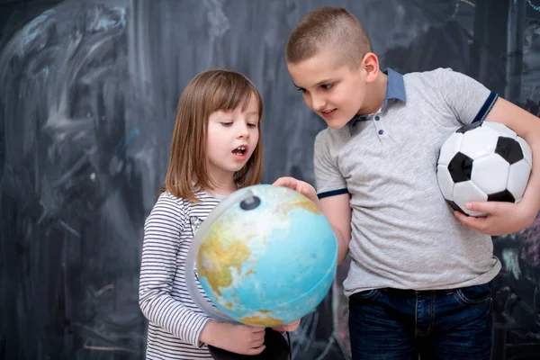 Boy and little girl using globe of earth in front of chalkboard — Stock Photo, Image