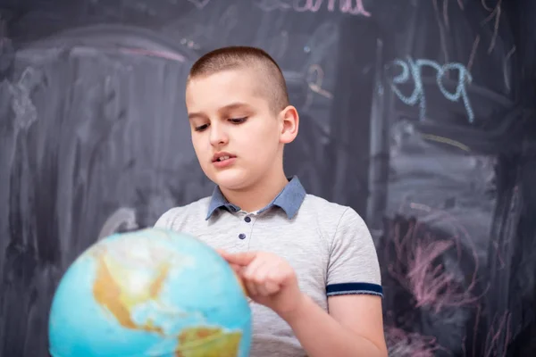 Boy using globe of earth in front of chalkboard — Stock Photo, Image