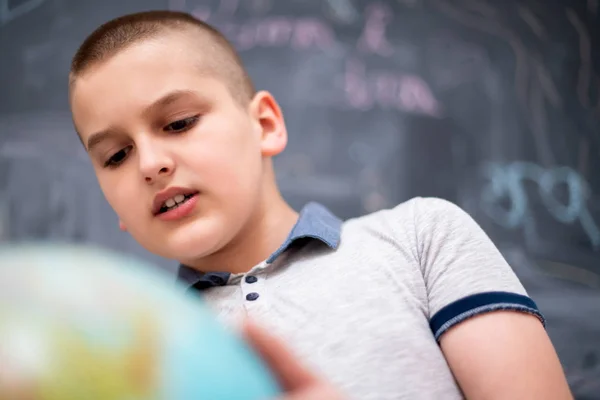 Boy using globe of earth in front of chalkboard — Stock Photo, Image