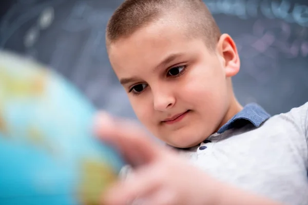 Menino usando globo de terra na frente do quadro — Fotografia de Stock