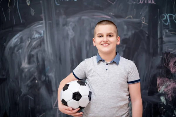 Χαρούμενο αγόρι που κρατάει μια μπάλα ποδοσφαίρου μπροστά από τον πίνακα — Φωτογραφία Αρχείου