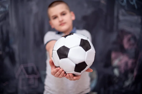 Menino feliz segurando uma bola de futebol na frente do quadro — Fotografia de Stock