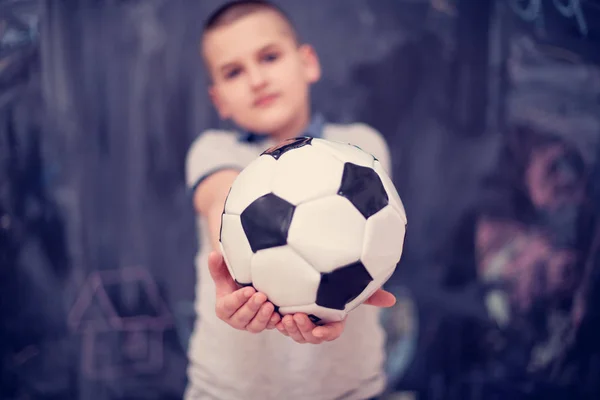 Niño feliz sosteniendo una pelota de fútbol en frente de pizarra — Foto de Stock