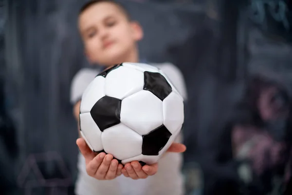 Niño feliz sosteniendo una pelota de fútbol en frente de pizarra — Foto de Stock