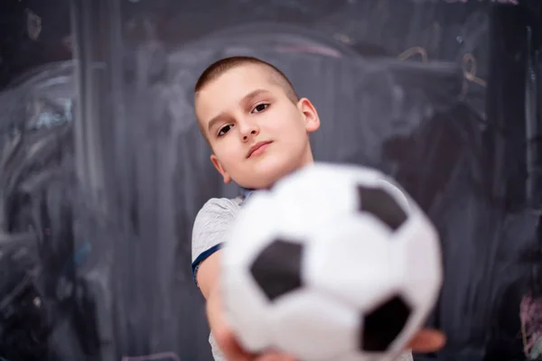 Niño feliz sosteniendo una pelota de fútbol en frente de pizarra — Foto de Stock