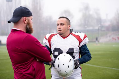 Amerikan futbolcu koçla strateji tartışıyor