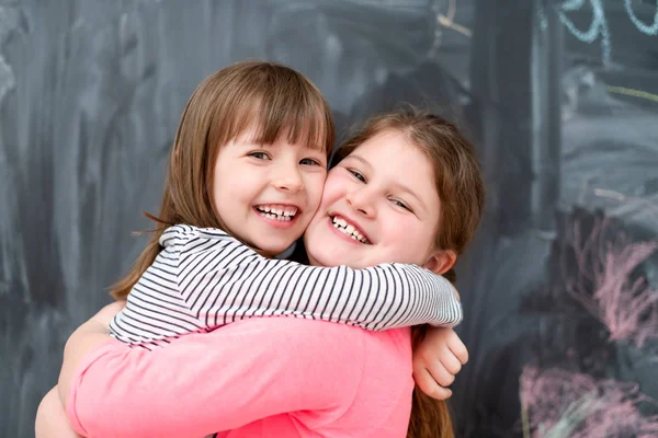 Kleine meisjes knuffelen in de voorkant van schoolbord — Stockfoto